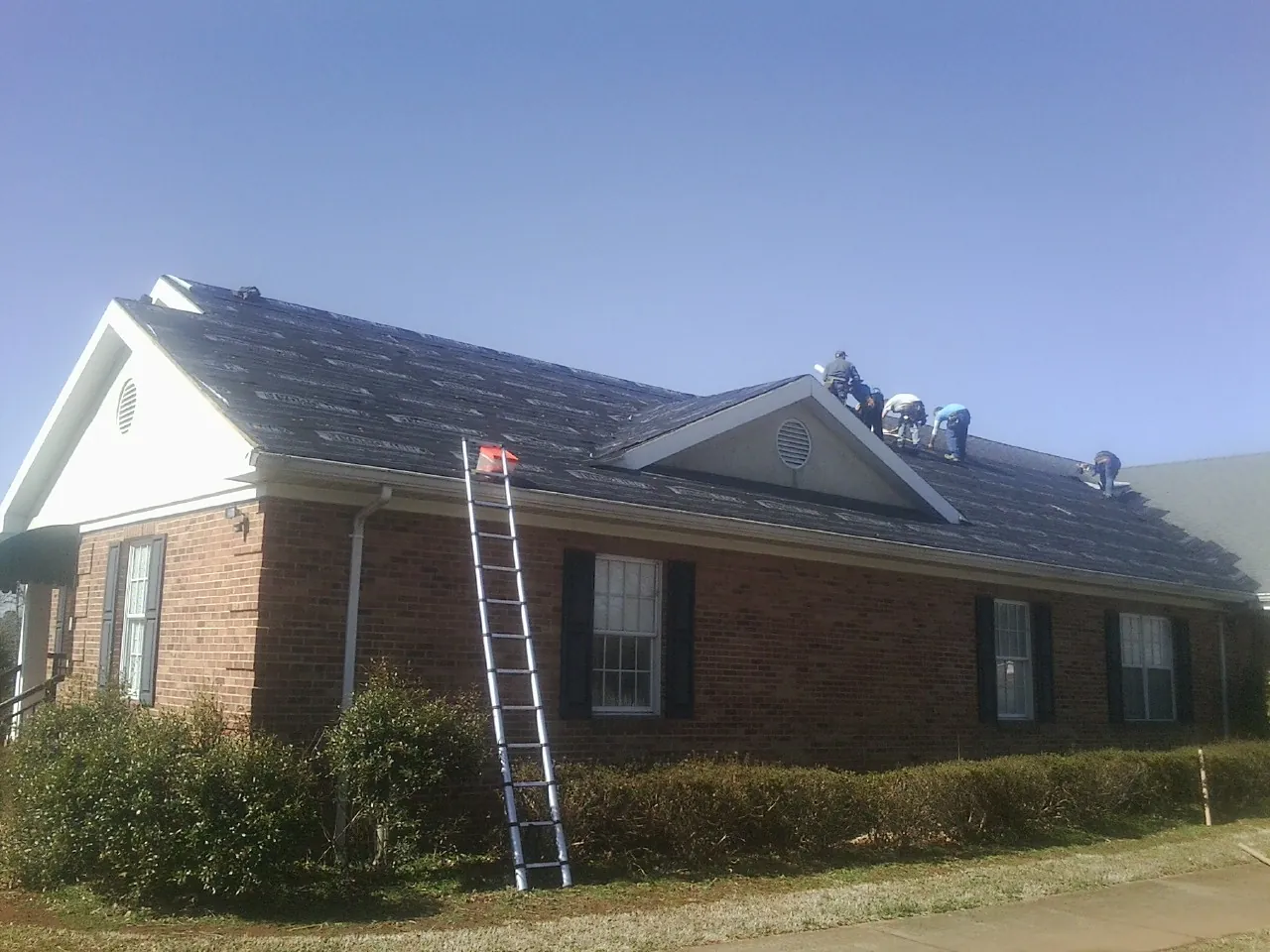 Crew tearing shingles off a brick ranch roof with a ladder set — Emergency Roof Repair work by our crew in Crisfield