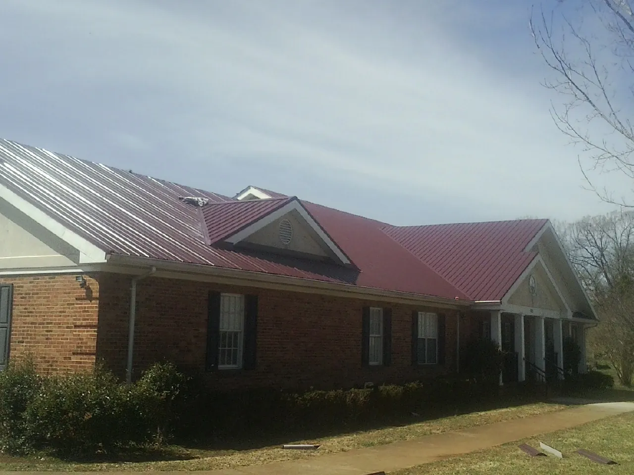 Red metal roof with gabled entries on a long brick building, from a Hail Damage Roof Repair job in Crisfield