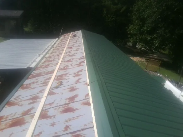 Old rusted panels beside newly installed green metal roofing — Wind Damage Roof Repair by Roofing Brothers in Crisfield