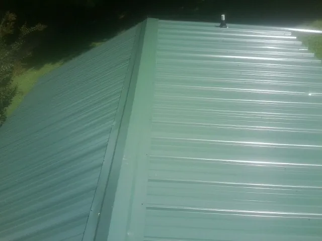 New green metal panels meeting at the ridge of a roof — Flat Roof Repair work by our crew in Crisfield