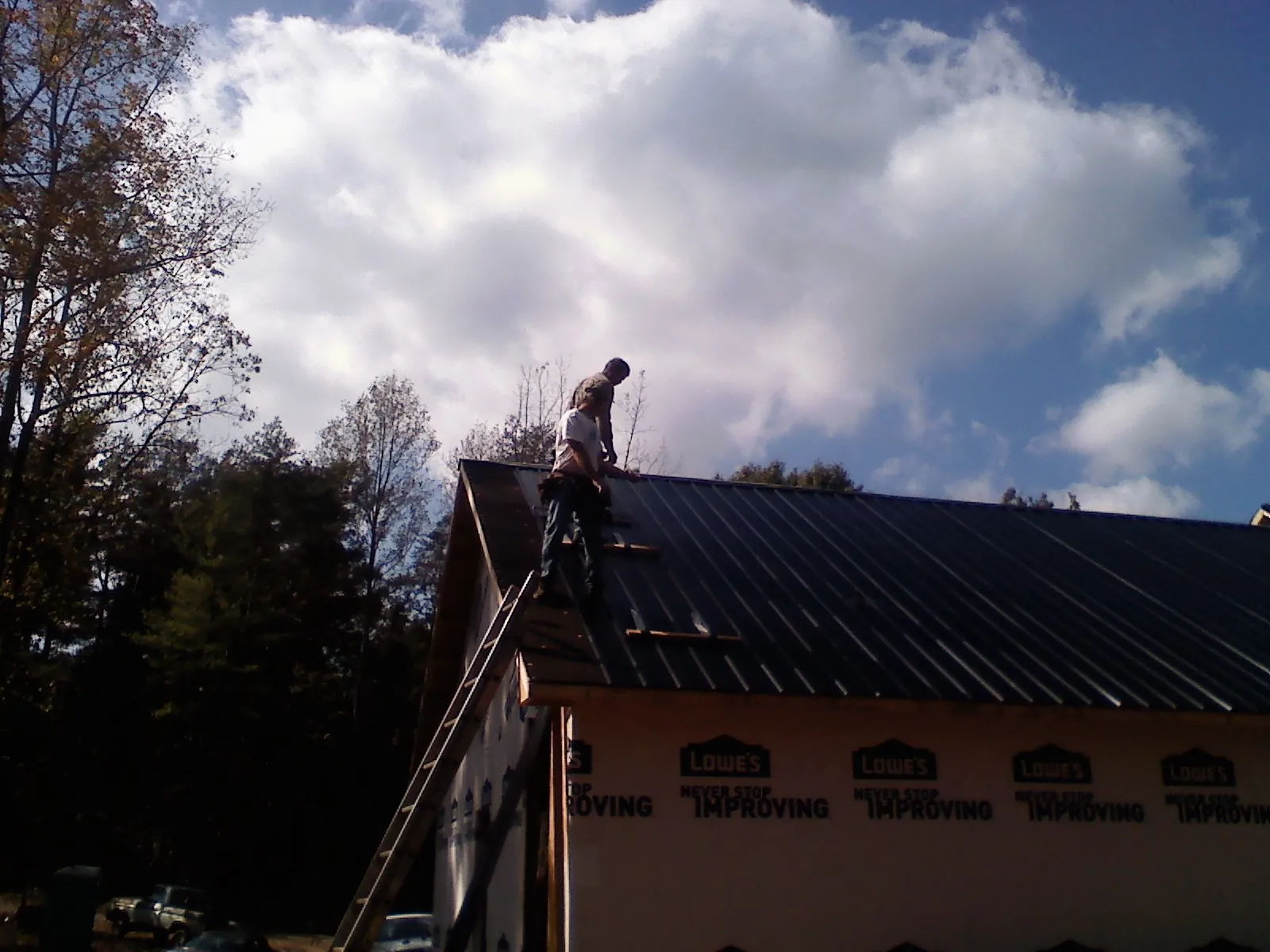 Roofer fastening dark metal panels high against a cloudy sky, from a Roof Inspection job in Crisfield