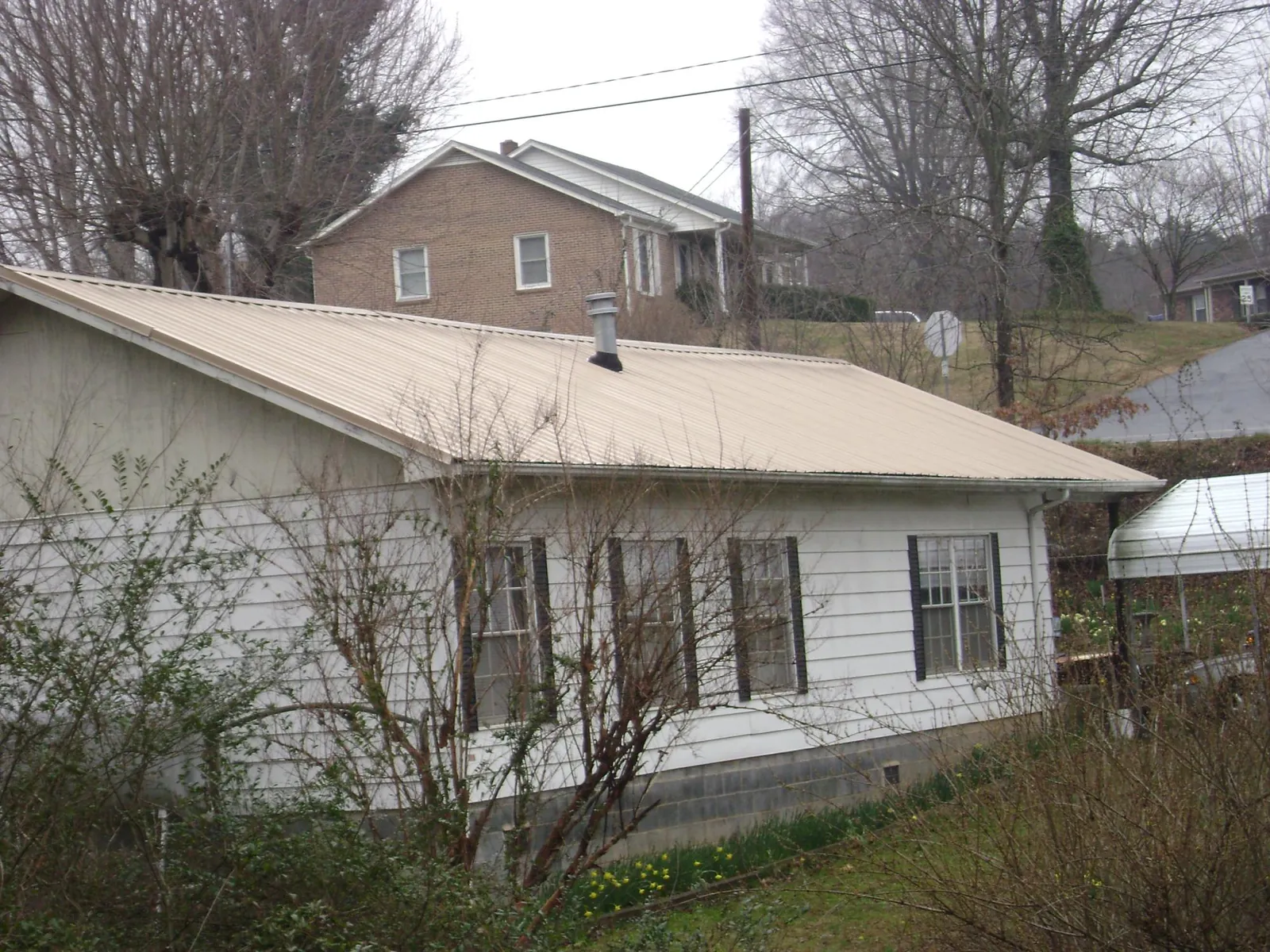 Tan metal roof on a white sided house set into a hillside — Commercial Roofing by Roofing Brothers in Crisfield